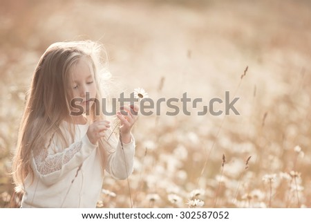 little girl with long blond hair standing in the field with daisies at sunset