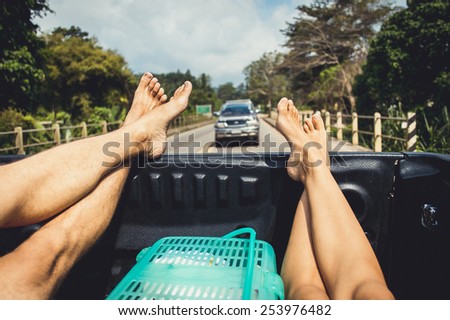 Legs of two hitchhiker man and woman traveling in pickup car with the road view on background