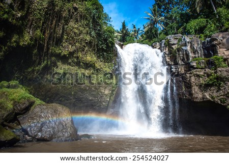 Waterfall and rainbow surrounded with green tropical forest and rocks, horizontal
