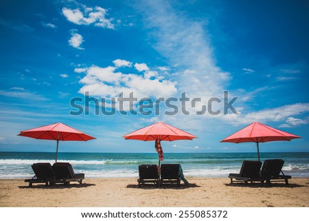 Three red sun umbrellas stay on yellow sand beach with blue sea and blue sky on background. Concept for rest, relaxation, holidays, spa, resort.
