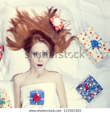 Redhead girl in bed with gifts. Photo in warm tone style.