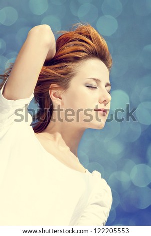 Portrait of redhead girl in white on blue sky with bokeh at background.