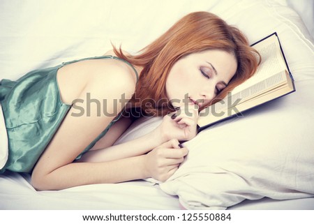 Pretty red-haired woman sleeping in the bed near book. Studio shot.