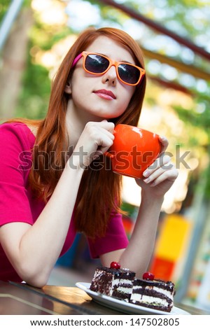 Style redhead girl with cup and cake sitting on the bench in the cafe