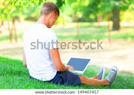 Teen boy with laptop in the park.