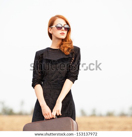 Redhead girl with suitcase at autumn field