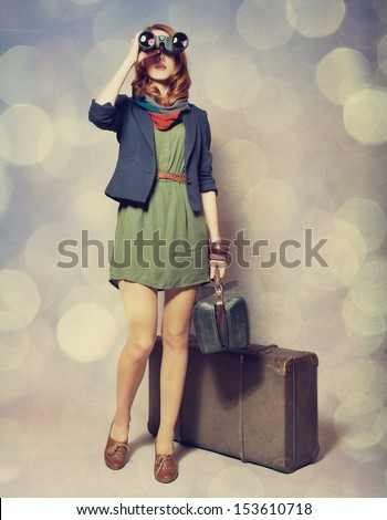 Redhead girl with binocular standing near the big suitcase