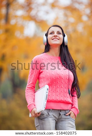 Portrait of a woman at outdoor with headphones and notebook.
