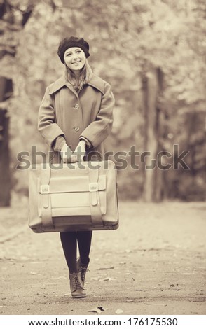 Redhead girl with suitcase at autumn outdoor. Photo in old color image style.