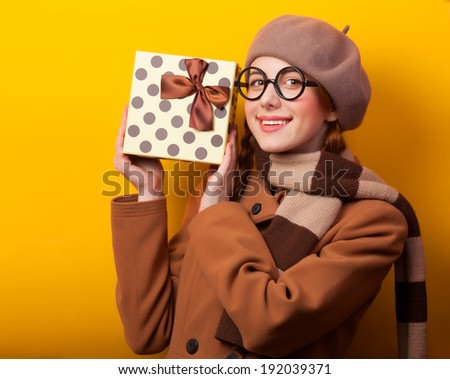 Redhead girl with gift box on yellow background.