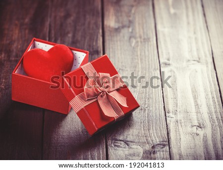 Red gift box with toy heart inside on wooden table. Photo in retro color image style.