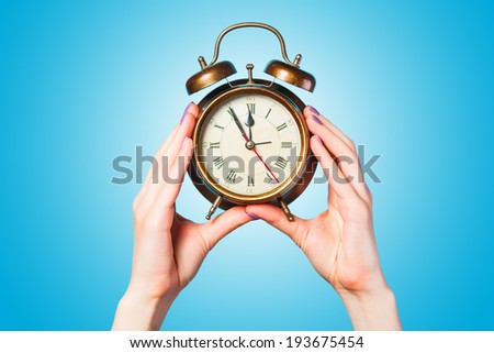 Hands holding alarm clock on blue background.