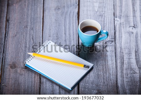 Cup of coffee witn notebook and pencil, on wooden table.