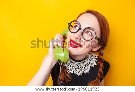 Redhead girl with green phone on yellow background.