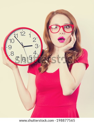 Surprised redhead girl with huge alarm clock on light background.