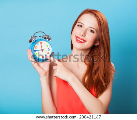 Smiling redhead women woth alarm clock on blue background.
