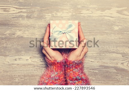Female hands holding gift on wooden table.