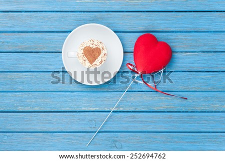 Cup of Cappuccino with heart shape symbol and toy on blue wooden background.