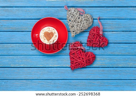 Cup of Cappuccino with heart shape symbol and toys on blue wooden background.