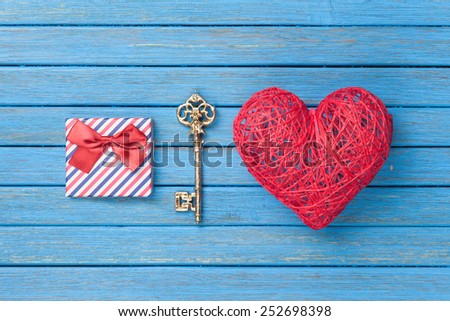 Heart shape toy with key and gift box on blue wooden background.