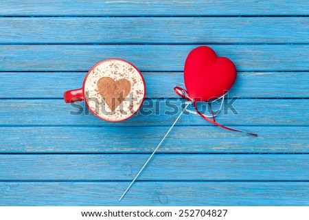 Cup of Cappuccino with heart shape symbol and toy on blue wooden background.