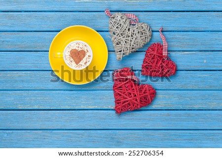 Cup of Cappuccino with heart shape symbol and toys on blue wooden background.