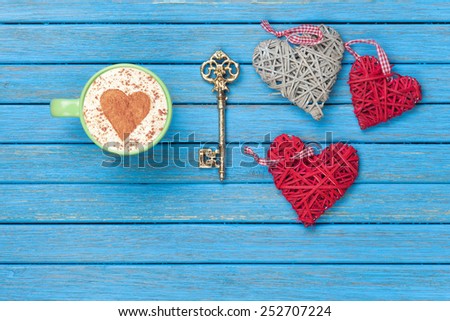 Cup of Cappuccino with heart shape symbol, key and toys on blue wooden background.