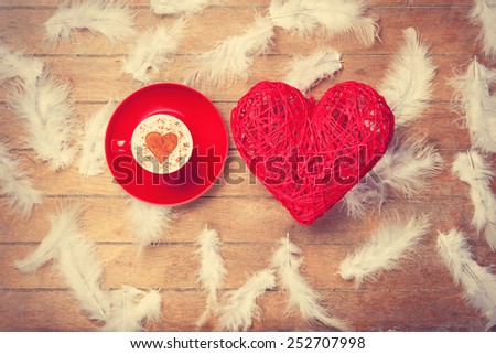 Toy heart and cup of coffee with heart shape and feathers on wooden background.