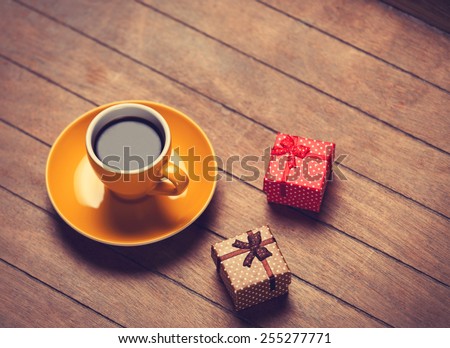 Cup of coffee and gift boxes on a wooden table. Photo in old color image style.