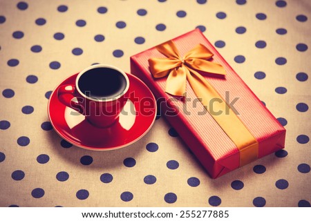 Cup of coffee and gift box on a polka dot background. Photo in old color image style.