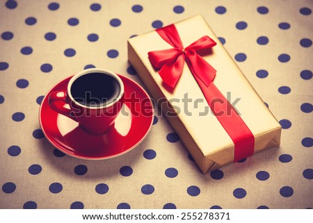 Cup of coffee and gift box on a polka dot background. Photo in old color image style.