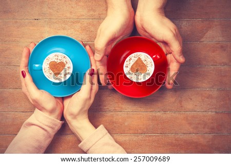 Women and man holding cups of coffee with heart shape symbol on a wooden background