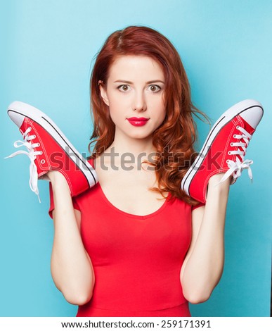 Surprised redhead girl in red dress with gumshoes on blue background.