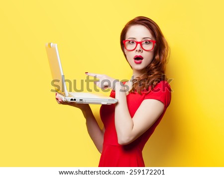Surprised redhead girl with laptop on yellow background
