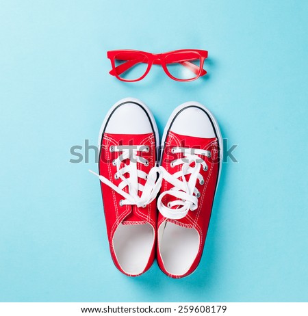 Red gumshoes with white shoelaces and glasses on blue background.
