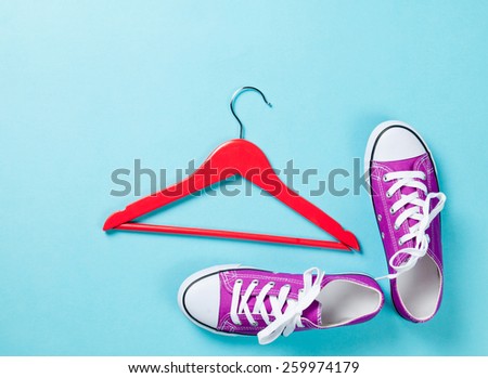 purple gumshoes with white shoelaces and red hanger on blue background.