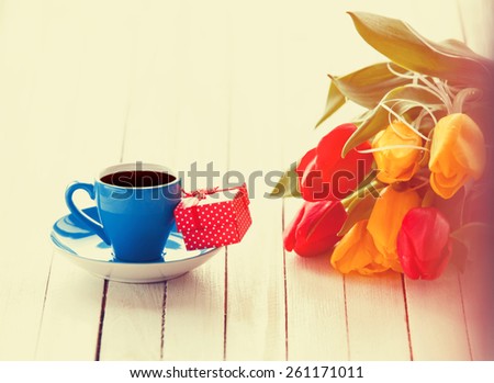 Cup of coffee and gift box with bouquet of tulips on white table.