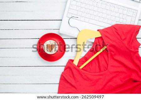 Cup of cappuccino with heart shape and computer with hanger on white background.