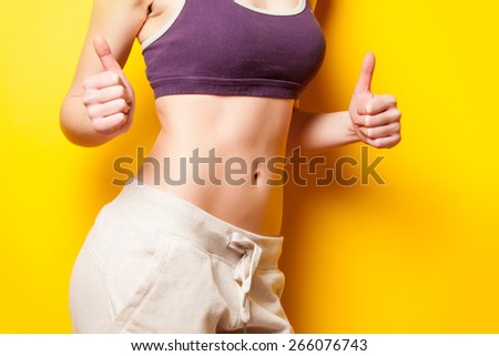 Woman showing her abs after weight loss on yellow background