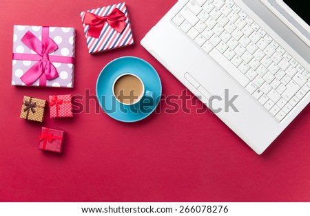 Cup of coffee and gift near computer on red background