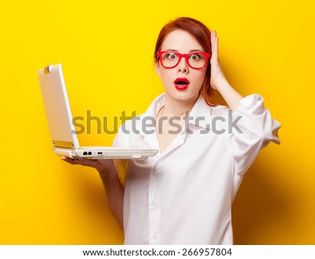 Surprised redhead girl in white shirt with computer on yellow background.