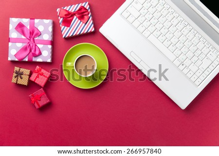 Cup of coffee and gift near computer on red background