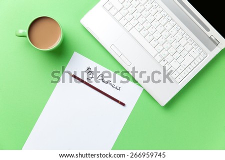 cup of coffee and computer with paper on green background