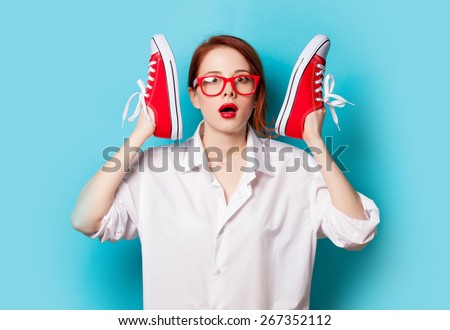 Surprised redhead girl in white shirt with gumshoes on blue background.