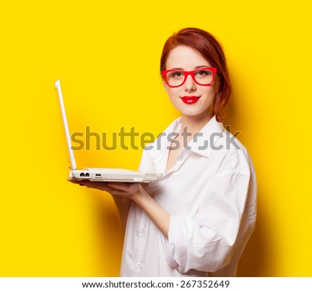 Happy redhead girl in white shirt with computer on yellow background.