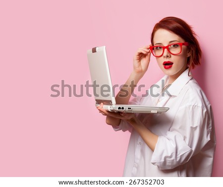 Surprised redhead girl in white shirt with computer on pink background.