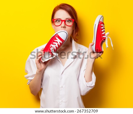 Surprised redhead girl in white shirt with gumshoes on yellow background.