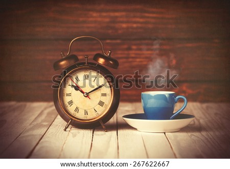 Cup of coffee and alarm clock on wooden table and background.