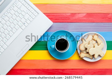 Cup of coffee with cookies and laptop on multicolored background