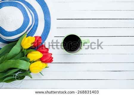 Cup of coffee with hat and tulips on white wooden table.